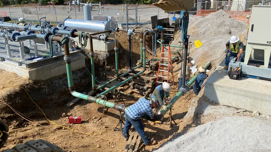 Crews welding a valve and piping assembly at a pipeline facility site