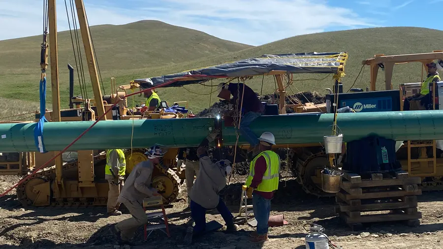 Crews welding a large-diameter pipeline joint under a canopy
