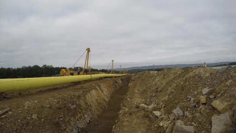 Pipe staged alongside a trench cut through rock