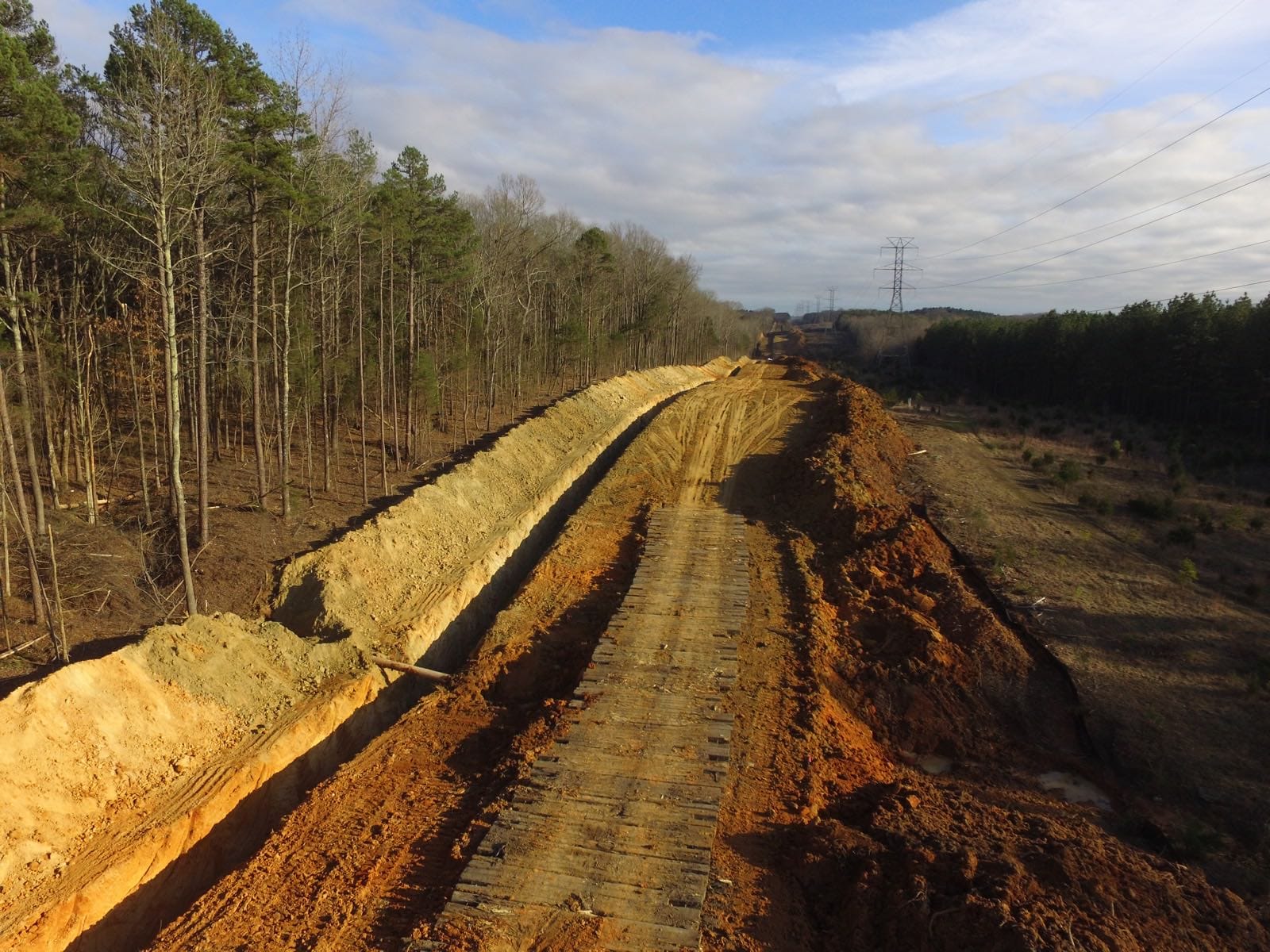 A graded right-of-way running cross-country toward transmission towers.